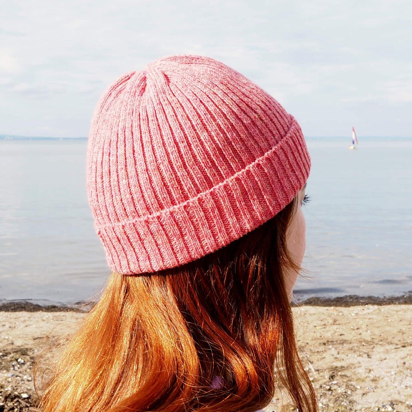 A woman wearing a pink ribbed beanie with a folded brim looks into the distance.