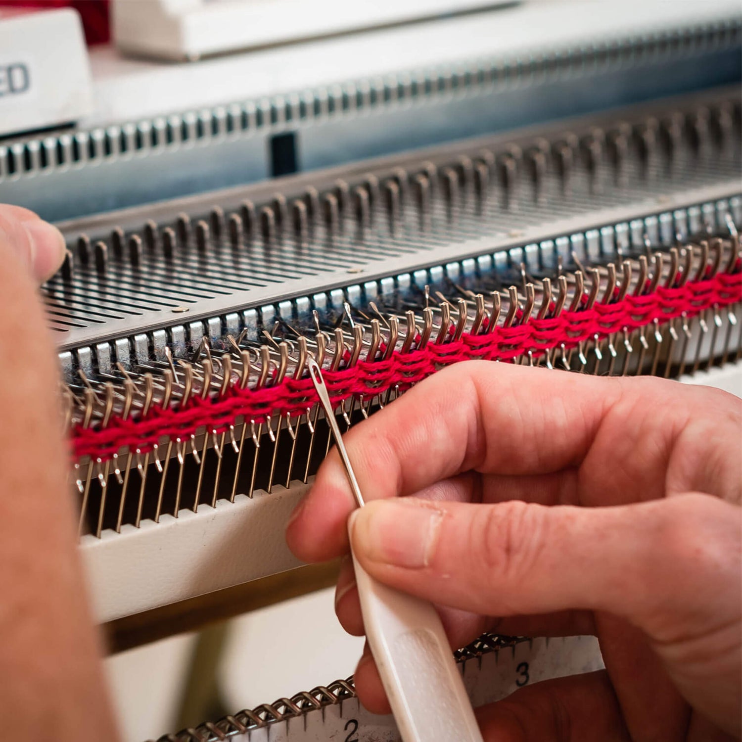 Hands work at a domestic knitting machine using pink yarn.