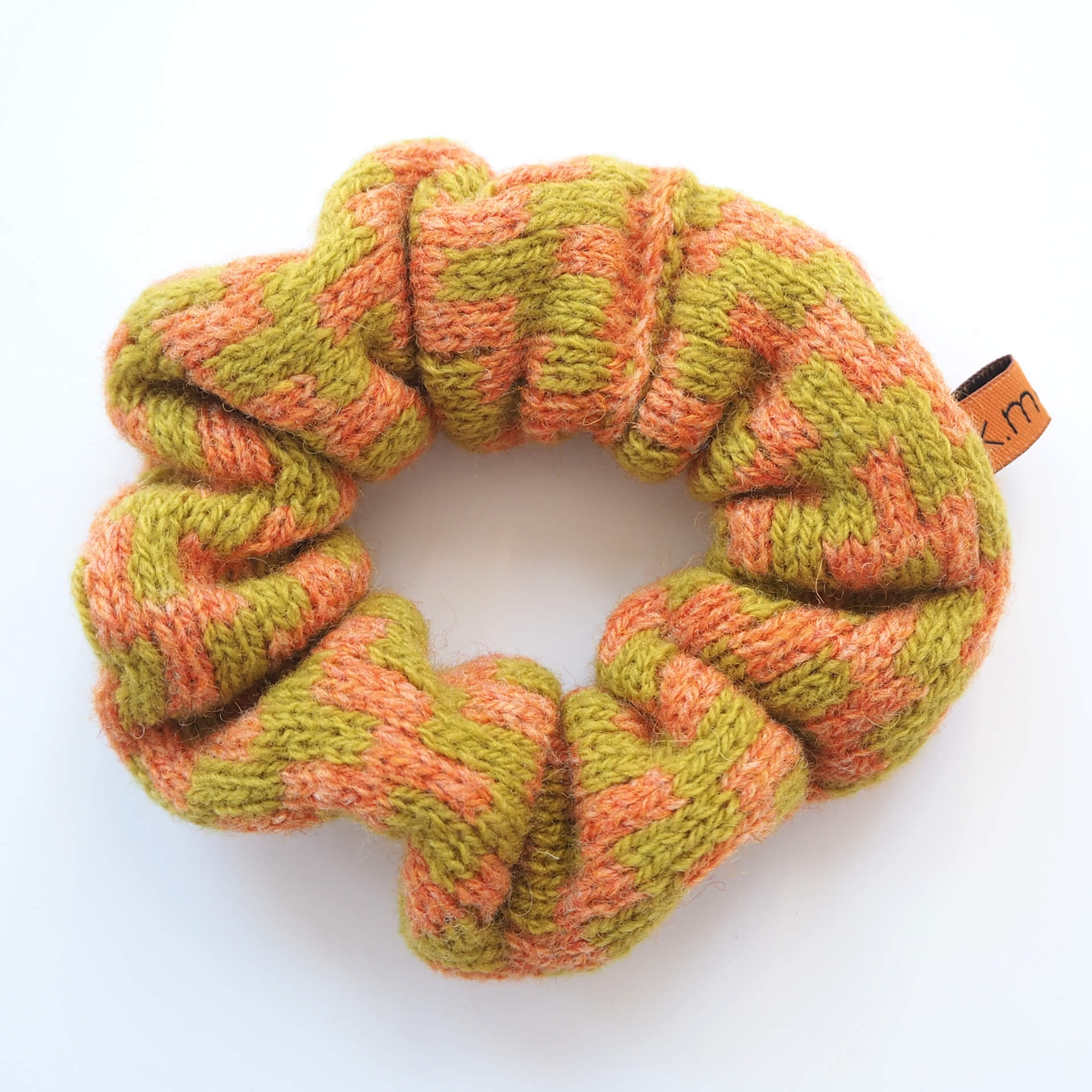 A knitted scrunchie with a thick zig-zag pattern by K.Moods. It is lime green and orange, and is on a white background.