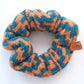 A knitted scrunchie with a thick zig-zag pattern by K.Moods. It is lime blue and orange, and is on a white background.