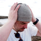 A man is putting on a grey ribbed beanie by K.Moods.