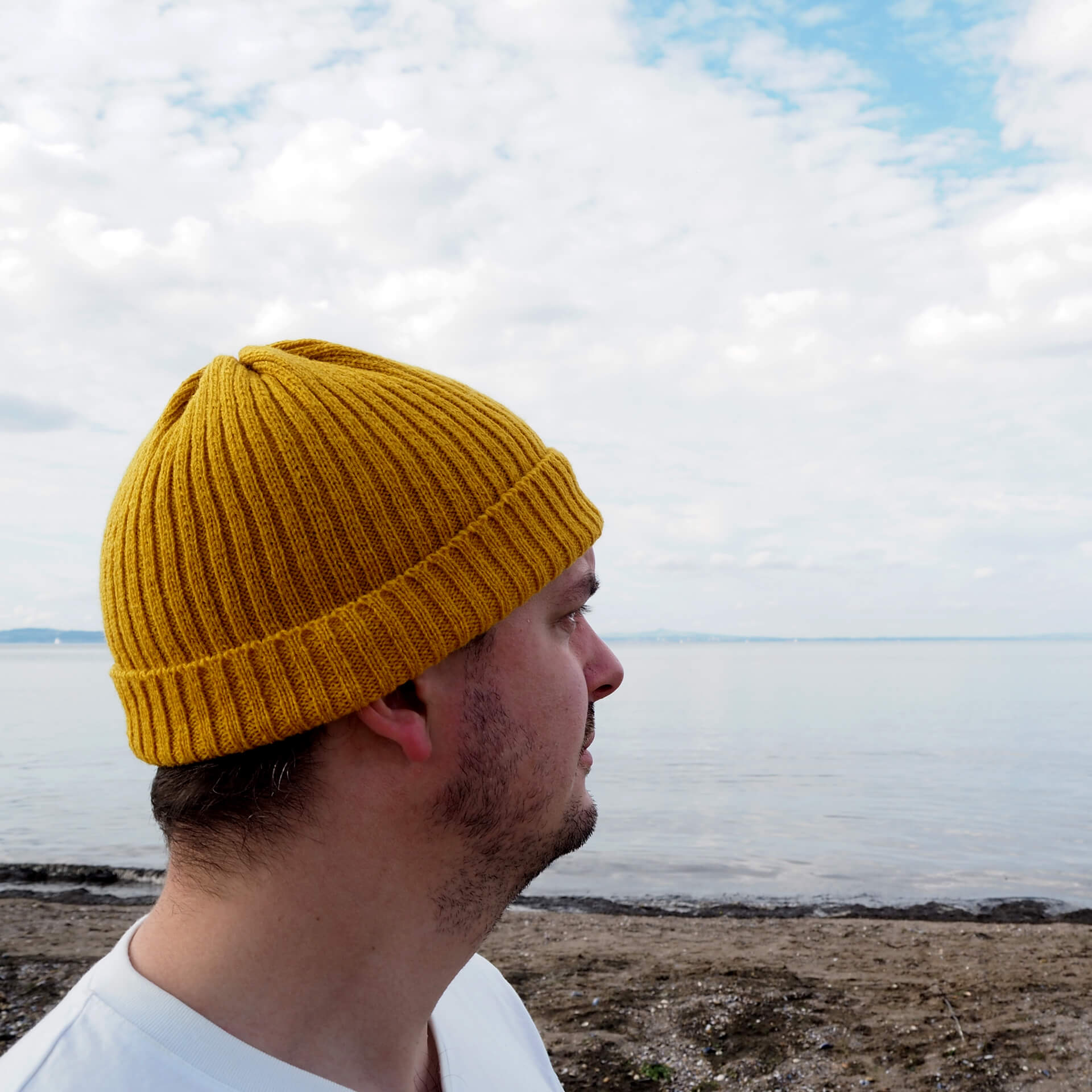 A man wearing a yellow ribbed beanie by K.Moods, looking out to the distance.
