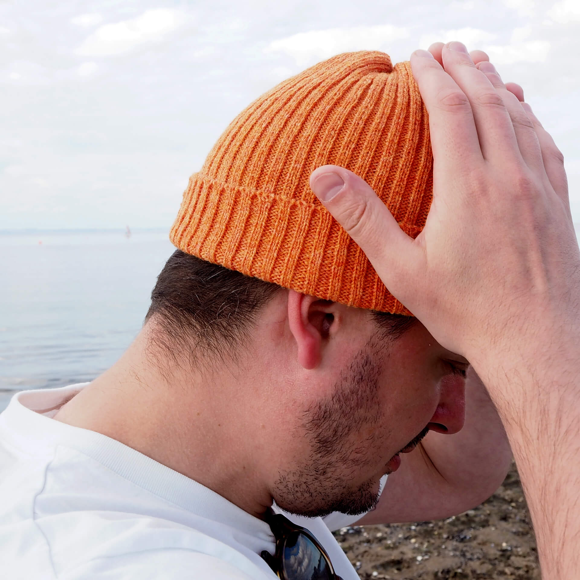 A man is adjusting an orange ribbed beanie by K.Moods.