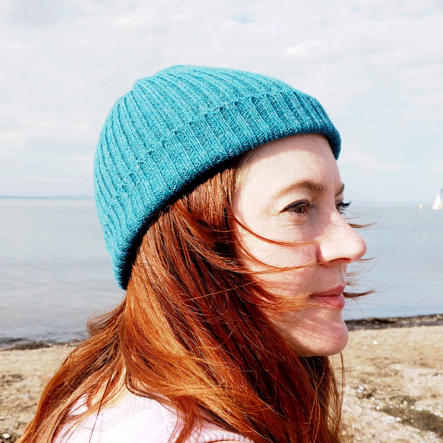 A profile view of a woman with red hair wears a blue ribbed beanie by K.Moods.