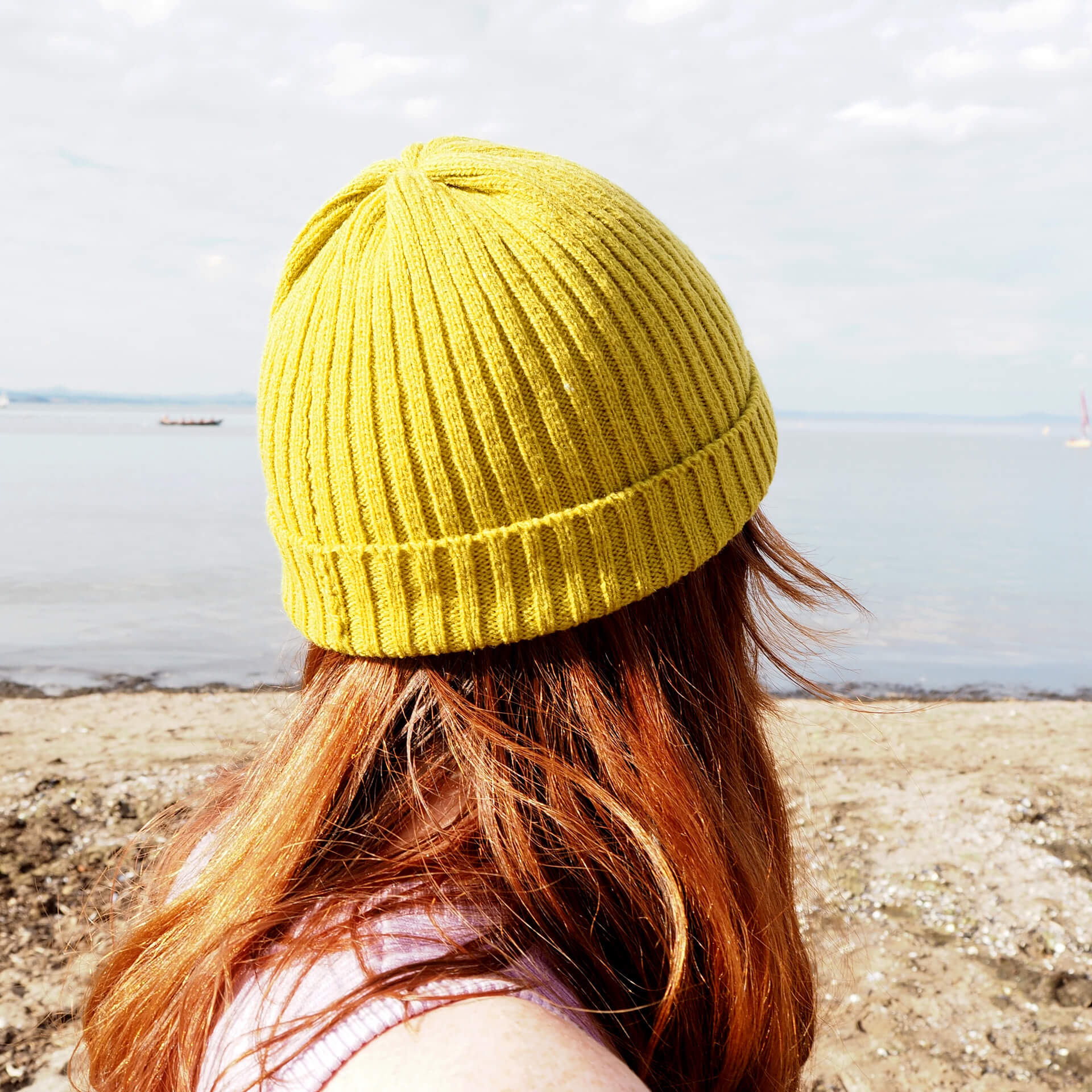 A woman looks into the distance while wearing a lime green ribbed hat by K.Moods.